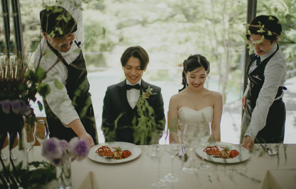 写真：スタッフふたりが料理を新郎新婦の前に置く様子